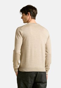 Maglione leggero beige con maniche lunghe, scollo rotondo e polsini a costine. Texture liscia con lievi variazioni tonali nel tessuto.