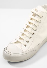 Sneaker alta bianca, tomaia in tela con lacci, occhielli in metallo, punta in gomma e parafango liscio. Design minimalista con una finitura testurizzata.