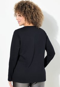 Schwarzes Langarmoberteil aus einem weichen Stoff, mit Rundhalsausschnitt und glatter, einfarbiger Textur. Keine sichtbaren Muster oder Akzente.