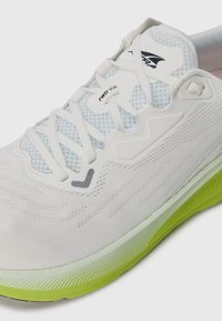 White running shoe featuring a mesh upper, textured midsole, and a bright green outsole. Notable brand logo and lace-up design.