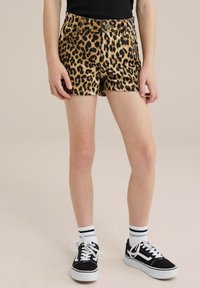 Traperice kratke hlače s leopard uzorkom, prilagođenog kroja, prednjim džepovima i metalnim dugmetom, uparene s crnim tenisicama i prugastim čarapama.