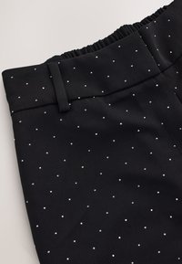 Black pants with a smooth texture, featuring a patterned design of small, silver dots. Elastic waistband and tailored structure evident.