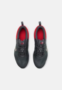 Baskets de sport grises avec texture en maille, doublure intérieure rouge, accents noirs et semelle blanche. Présente un tirant et des lacets traditionnels.