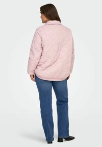 Gepolsterte, hellrosa Jacke mit gesteppter Gestaltung, hohem Kragen und lockerem Schnitt, kombiniert mit blauen Jeans mit geradem Bein und schwarzen Stiefeletten.