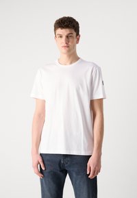 White cotton t-shirt with a round neckline and short sleeves. Features a logo patch on the left sleeve and a regular fit design.