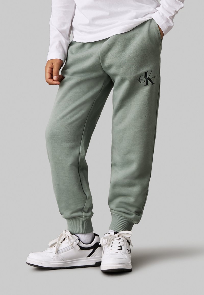 Pantaloni della tuta verdi realizzati in tessuto morbido, con vita elastica e caviglie a polsino. Presentano un logo nero sulla coscia sinistra.