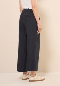 Brede marineblauwe broek gemaakt van zachte stof met een textuurafwerking. Heeft een elastische tailleband en zijzakken. Casual witte sneakers.