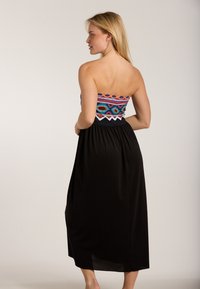 Trägerloses Kleid mit buntem besticktem Oberteil, schwarzem fließendem Rock und Spitzensaum. Leichter Stoff, knielange Länge, lockere Passform.