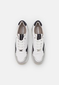 Vita och marinblå sneakers med perforerat läder och anpassade detaljer i mocka. Har snörning, vadderad krage och texturerad gummisula.