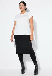 Witte T-shirt met korte mouwen en een grafische print, gecombineerd met een zwarte rok met kleine stippen en zwarte enkelboots met studs.