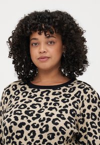 Beige genser med svart leopardmønster, med rund halsutskjæring og ribbestrikkede kanter. Teksturen ser ut til å være strikket og myk.