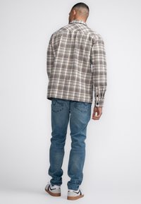 Kariertes Flanellhemd in Beige und Braun mit zwei Brusttaschen, kombiniert mit hellblauen Jeans und weißen Sneakers mit schwarzen Akzenten.