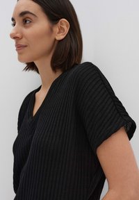 Schwarzes Stricktop mit V-Ausschnitt und kurzen Ärmeln in Rippstruktur. Das Design umfasst horizontale Streifen und aufgerollte Ärmelabschlüsse.