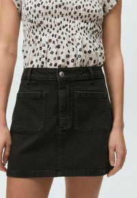 Jupe en denim noir au design ajusté, avec des poches avant et une fermeture à bouton à l'avant. Le matériau a une légère extensibilité et une texture lisse.