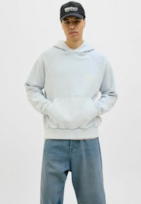 Light blue hoodie with a front pocket and ribbed cuffs, featuring a small embroidered logo. Paired with medium blue denim jeans.