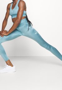 Ensemble de brassière de sport et de leggings turquoise, fabriqué dans un matériau extensible et lisse. Comprend des accents de logo subtils et un design ajusté.