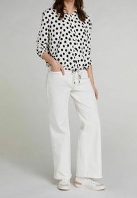 Pantaloni larghi in cotone bianco abbinati a una camicetta a bottoni bianco e nero con pois. La camicetta ha una vestibilità comoda e le maniche arrotolate.