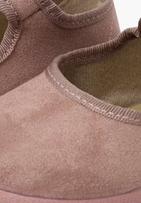 Zapatillas rosas sin cordones hechas de un tejido suave, con una textura lisa, forma redondeada y un sutil detalle de costura en los bordes.