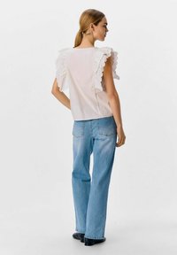 Weiße Bluse mit rüschierten, gewellten Ärmeln, kombiniert mit hellblauen geraden Jeans. Glatter Stoff und schlichtes Design.
