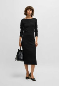 Pull en tricot noir à manches longues et encolure bateau, associé à une jupe noire mi-longue. Les accessoires comprennent un sac fourre-tout noir et des chaussures noires.
