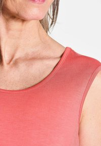 Korallenfarbenes ärmelloses Shirt mit glatter Textur, rundem Ausschnitt und tailliertem Design, das den Bereich des Schlüsselbeins betont.