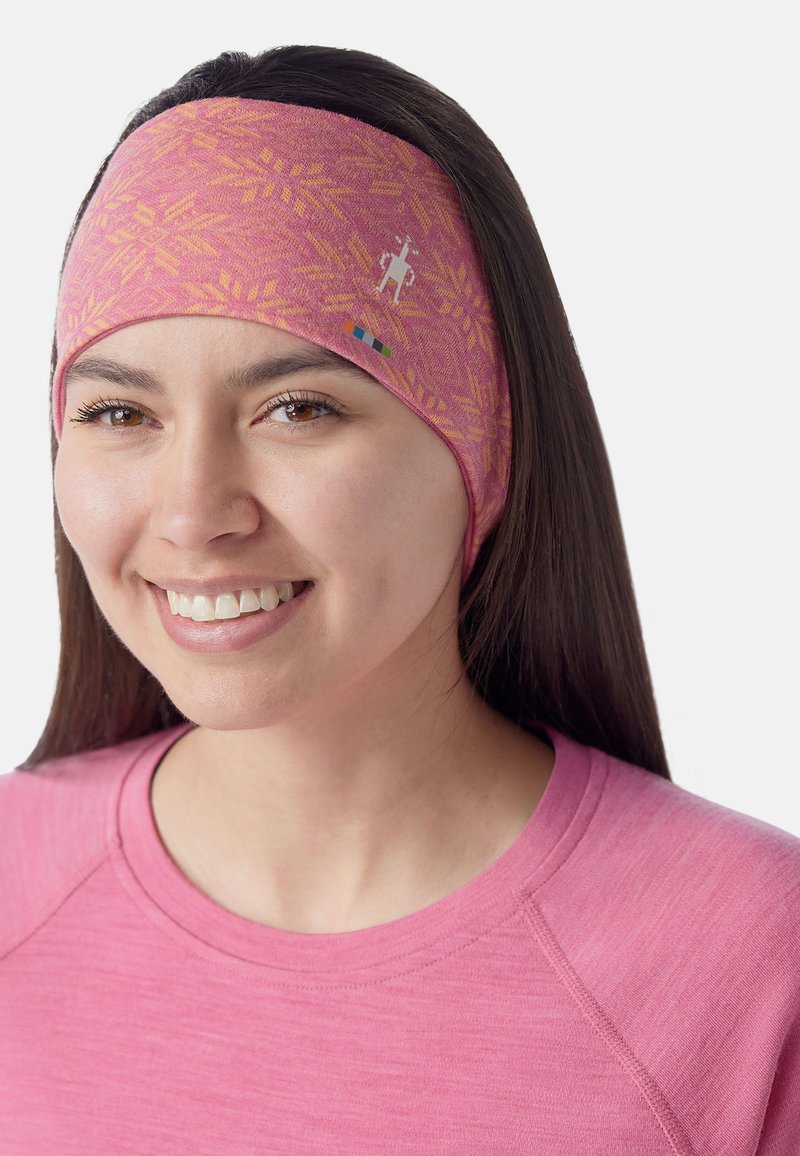 Fascia di stoffa morbida di colore rosa con un motivo geometrico e un logo ricamato. Indossata con una maglia rosa coordinata.
