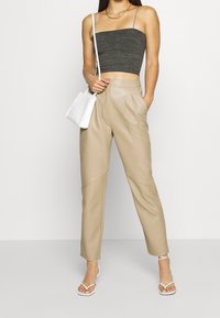 Pantaloni beige in ecopelle con pieghe, abbinati a un crop top grigio scuro a coste. Mini borsa bianca e sandali bianchi con cinturini completano l'outfit.