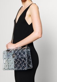 Borsa trasparente con un motivo trapuntato, borchie argentate e tracolla a catena. Il materiale trasparente mette in risalto il design e la struttura unici.
