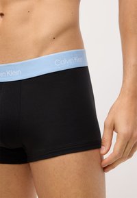 Čierne bavlnené boxerky s svetlomodrým elastickým pásom so značkou "Calvin Klein". Hladká textura, priliehavý strih, minimalistický dizajn.