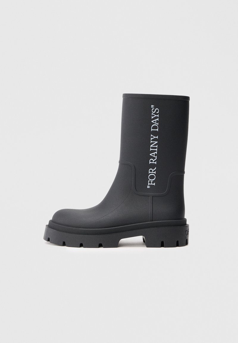 Botte de pluie en caoutchouc noire avec une semelle épaisse et un texte en relief "POUR LES JOURS DE PLUIE". Texture lisse, tige haute et bords renforcés.