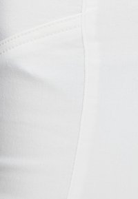 Vit denimtyg med subtil textur, med böjda sömmar och ljusa sömnadsdetaljer, som ger en jämn yta.