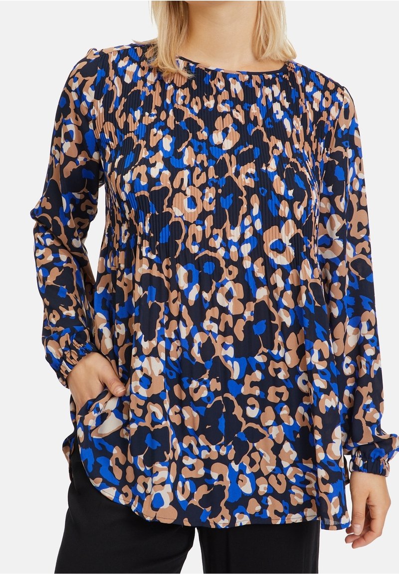 Blouse à manches longues avec imprimé léopard bleu, beige, noir et blanc, avec un col rond et des détails plissés.