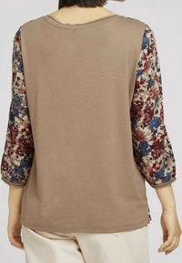 Långärmad topp med en beige kropp och ärmar med blommönster i blått, rött och kräm-vitt. Har en avslappnad passform och rund halsringning.