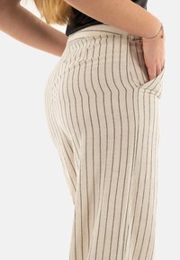 Pantaloni a palazzo a righe beige con strisce verticali blu, dotati di tasche laterali e vita alta, realizzati in un morbido tessuto testurizzato.