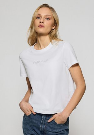 Camiseta blanca de algodón con un cuello redondo, mangas cortas y un ajuste cropped. Presenta un sutil texto "Polo Club" en gris en el pecho.