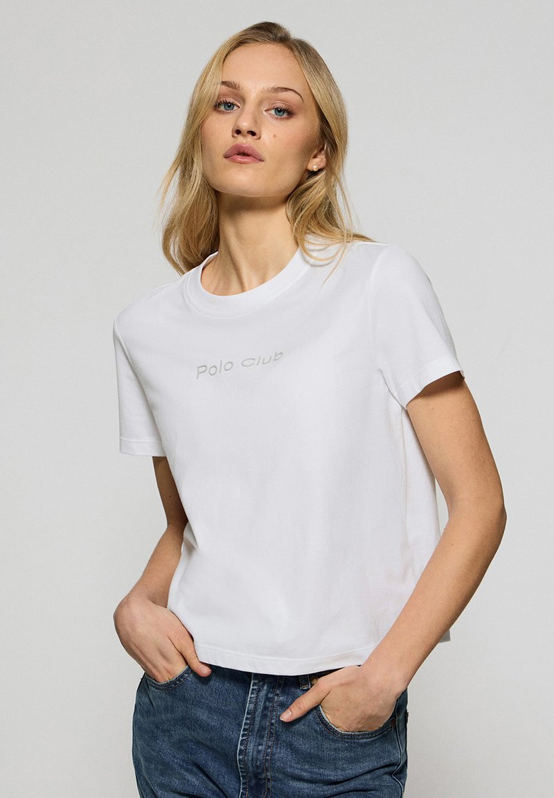 Vit bomulls t-shirt med rund halsringning, korta ärmar och en kort skuren passform. Har diskret "Polo Club" text i grått över bröstet.