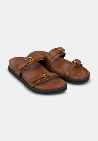Sandalias de imitación de cuero marrón con dos correas ajustables que presentan hebillas en tono dorado, una plantilla contorneada y una suela de goma negra.
