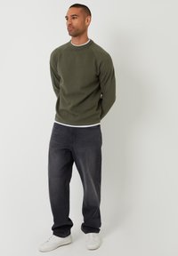 Olijfgroen fleece sweatshirt met ronde hals, geribbelde manchetten en zoom. Gepaard met donkergrijze jeans en witte sneakers.
