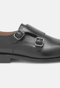 Chaussure en cuir noir au fini lisse, dotée de deux boucles argentées ajustables, d'une silhouette élégante et d'un petit talon empilé.