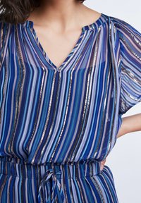 Blusa a righe blu con strisce verticali in diverse tonalità di blu e dettagli dorati, con scollatura a V e maniche corte. Morbida al tatto.