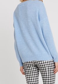 Pull bleu duveteux avec une coupe décontractée et un ourlet côtelé, associé à un pantalon à carreaux noirs et blancs. Accent sur la texture douce et le contraste des couleurs.