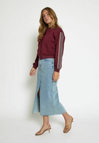 Burgundy cropped jacket with striped sleeve accents, paired with a light blue denim maxi skirt featuring a front slit, and nude heeled sandals.