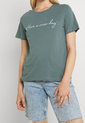 Zielony bawełniany t-shirt z krótkimi rękawami, okrągłym dekoltem i białym, kursywnym napisem "Have a nice day!" na przedzie. Niebieskie szorty jeansowe.