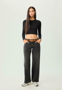 Top nero corto a maniche lunghe abbinato a jeans larghi grigio scuro e una cintura marrone. Scarpe atletiche argento completano l'outfit.