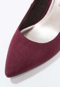 Burgundské semišové lodičky s špičatou špičkou, hladkým stříbrným interiérem a elegantním siluety; obsahují jemné švy.