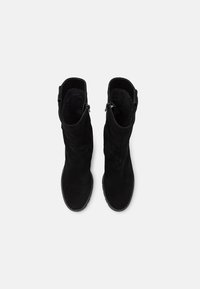 Svarta mockastövlar med en mjuk textur, i knähöjd, och med dragkedjor på sidorna. Sulorna är platta med ett minimalt mönster.