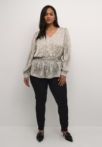 Blusa grigia chiara con motivo, scollatura a V, vita elasticizzata e maniche lunghe; abbinata a pantaloni neri slim-fit e ballerine nere.