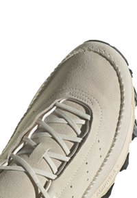 Beige mockasinsneakers med texturerad ovandel, platta snören och svart gummisula. Har förstärkt sömnad och präglade varumärkesdetaljer.