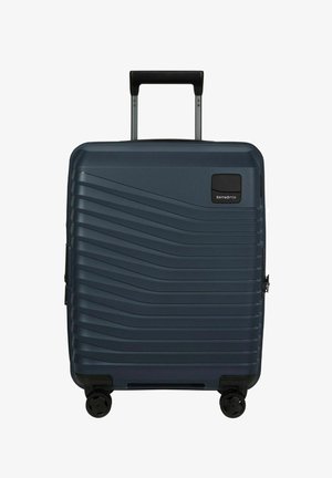 Valise rigide bleu foncé avec des rainures diagonales, quatre roues noires, poignée noire extensible et logo Samsonite en haut à droite.
