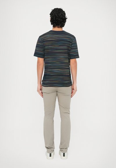 Rövid ujjú csíkos ing fekete alapon, színes vízszintes vonalakkal. Világos bézs nadrággal és fehér tornacipővel viselve.